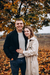 Fototapeta premium A couple hugging under a yellow-leaved autumn tree. Romantic walk in the fall park, warm atmosphere, love, and harmony surrounded by colorful foliage.