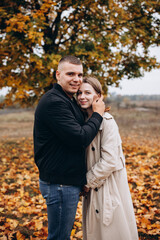 Fototapeta premium A couple hugging under a yellow-leaved autumn tree. Romantic walk in the fall park, warm atmosphere, love, and harmony surrounded by colorful foliage.