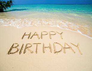 A cheerful birthday message is written in the smooth golden sand of a tropical beach, with turquoise waves gently rolling in under a clear blue sky.