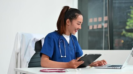 Asian doctor using tablet and laptop in medical office. Concept of healthcare, telemedicine, diagnostics, and medical technology. - Powered by Adobe