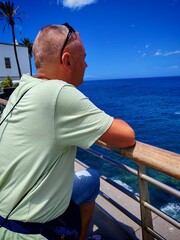 Adult male contemplating the sea view leaning on a railing, on a beautiful sunny day.view of a man...