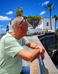 Adult male contemplating the sea view leaning on a railing, on a beautiful sunny day.view of a man...