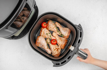 Raw chicken drumsticks with herbs and tomatoes in air fryer basket ready for cooking on white kitchen table. top view. copy space.