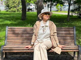 middle-aged Middle-aged blonde girl sits in a park on a bench and looks at the sun, enjoys spring.