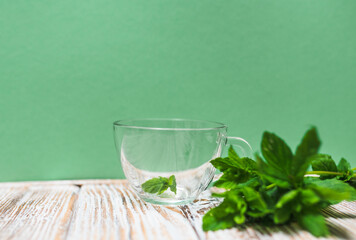 Tea cup with fresh mint leaves on a table on a green background with copy space. Health benefits of peppermint tea concept.