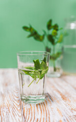 A glass with fresh mint leaves water on a table on a green background with copy space. Health benefits of peppermint water  concept.