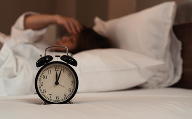 Insomnia or Sleep changes and disorders in adult concept.Alarm clock time at midnight with blurry women lay down awake.
