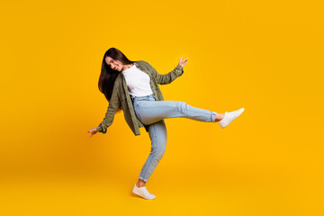 Dynamic young female in casual attire striking a playful pose against a vibrant yellow backdrop