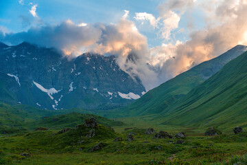 Fototapeta premium mountain landscape with clouds und green grass at sunset