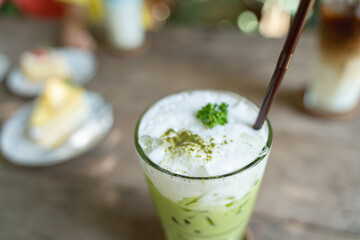 Close-up of iced matcha green tea latte with whipped foam and a sprig of parsley, served in a glass with a straw on a rustic wooden table.