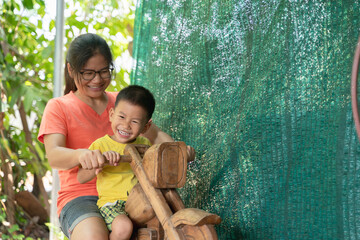Happy mother and young boy smiling while playing together on a wooden rocking horse outdoors, enjoying quality family time.