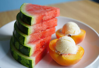 Delightful summer treat with perfectly stacked watermelon slices alongside two halved peaches topped with a scoop of creamy vanilla ice-cream