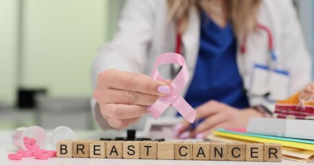 Woman doctor holds pink ribbon in hand to show support for Breast Cancer awareness shown on cubes. Physician emphasizes value of regular screenings - Powered by Adobe
