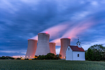 A small rural chapel stands in striking contrast to the massive cooling towers of a nuclear power...