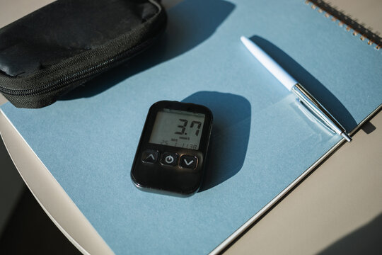 Close-up of a glucose meter with a low sugar index reading on the screen on a  table with notepad and pen