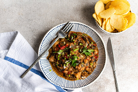 Overhead view of a Traditional Georgian chicken and tomato chakhokhbili dish with a bowl of ridged potato crisps