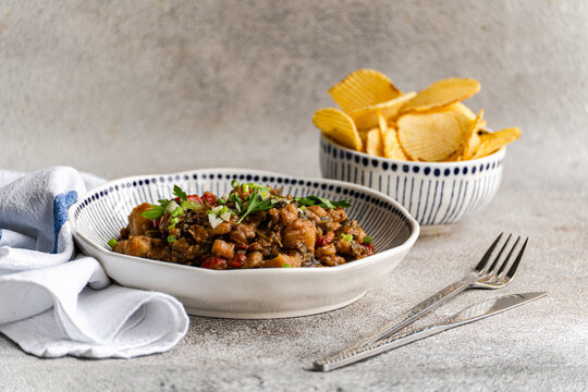 Close-up of a Traditional Georgian chicken and tomato chakhokhbili dish with a bowl of ridged potato crisps