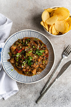 Overhead view of a Traditional Georgian chicken and tomato chakhokhbili dish with a bowl of ridged potato crisps