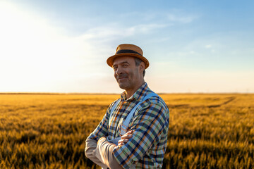 Portrait of smiling male farmer standing in wheat field at sunset looking at camera.