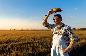 Portrait of adult male farmer standing in wheat field at sunset.