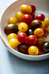 Assorted cherry tomatoes in ceramic bowl on blue surface