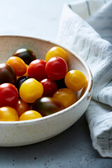 Assorted cherry tomatoes in ceramic bowl on blue surface