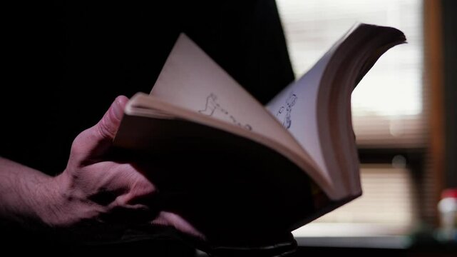 A close-up shot of hands carefully opening a book. The pages are visible, suggesting the beginning of reading or study. The focus is on the act of opening