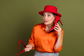 Confident woman with stylish red hat, holding a high heel shoe near her ear, presenting a quirky...