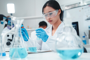 Young Asian female scientist in lab coat and safety goggles conducting chemical experiment with...