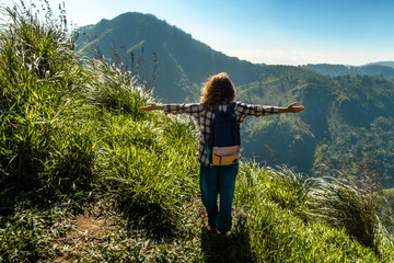 Adventure, summer tourism concept. Female tourist standing on top of mountain admiring beautiful scenic mountain landscape