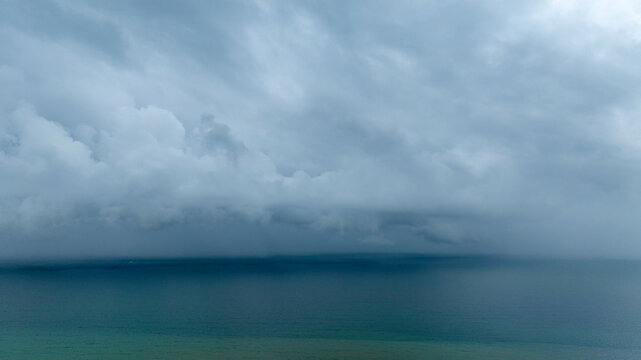 Aerial view of ocean on a cloudy and rainy day. There are clouds in the dark sky.