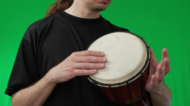 A man demonstrates playing a djembe drum against a vivid green screen background, perfect for compositing with various settings and themes