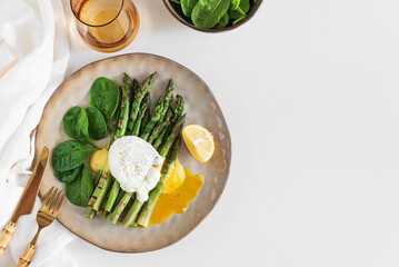 Poached egg with grilled asparagus, spinach, and hollandaise sauce on white table. Top view