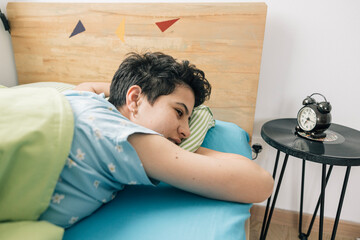 Teenager girl waking up and looking at alarm clock in bedroom