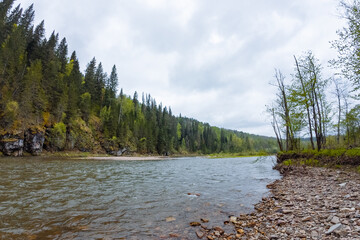 The Serene River Landscape is beautifully surrounded by lush green forests and rocky shores,...