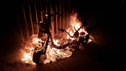 a stolen dumped moped on fire and burning next to a fence with flames roaring