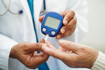 Asian doctor using digital glucose meter for check sample blood sugar level to treatment diabetes.