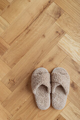 Cozy fur slippers on wooden oak parquet floor top view. Comfort home concept.