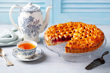 Berry sweet pie with cup of tea and teapot. Blue background. Close up.