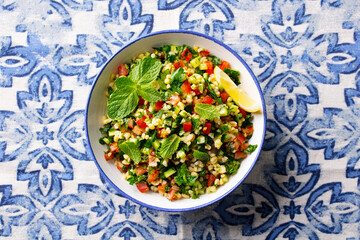 Tabbouleh salad in a bowl. Blue azulejo background. Close up. Top view.