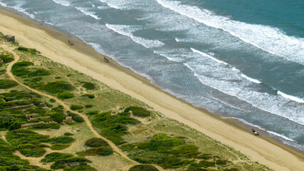 Aerial view of a beach with rough sea. On the beach there is a horse with a person while riding.