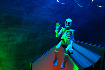 Halloween Stories.Skeleton Toy Sitting on Book with Lights. Book, skeleton and glowing garland. 
