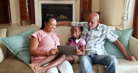 Diverse grandparents and granddaughter using tablet together on couch, enjoying family time - Powered by Adobe