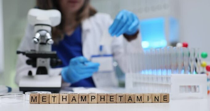 Text Methamphetamine on wood cubes in medical lab. Female scientist prepares sample of white powder drug for analysis under microscope in criminal lab