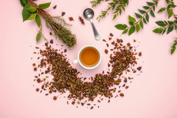 Herbal tea cup with dried leaves and fresh herbs on pink background, peaceful and natural