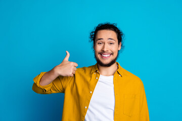 Smiling man in yellow shirt showing thumbs up against blue background symbolizing positivity and...