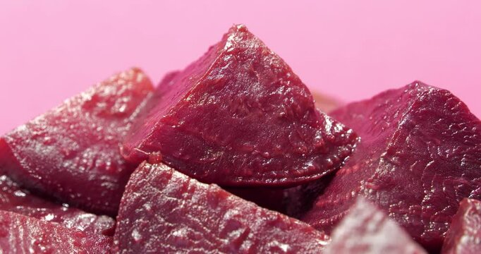 Red boiled beetroot cut into pieces rotates on pink background, close-up shot video