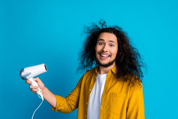 Cheerful man holding a hairdryer with wild hair against a bright background, expressing joy and a...