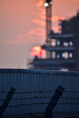 Close-up of metal corrugated board with sunset background and construction site. Fence from corrugated board. Texture of metal fence. For background use.