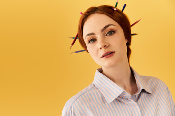 Creative young woman with colorful pencils styled in her hair against a vibrant yellow backdrop